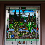 "An intricately designed stained glass window featuring Canada's native flora and fauna, evoking the landscape and cultural heritage of Canada, nestled in the frame of a charming heritage home."