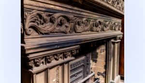 "Close-up view of an intricate antique fireplace in a heritage home, showcasing the detailed stone or wood carvings, with visible testament to unique personal elements and architectural trends of its era."