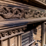 "Close-up view of an intricate antique fireplace in a heritage home, showcasing the detailed stone or wood carvings, with visible testament to unique personal elements and architectural trends of its era."